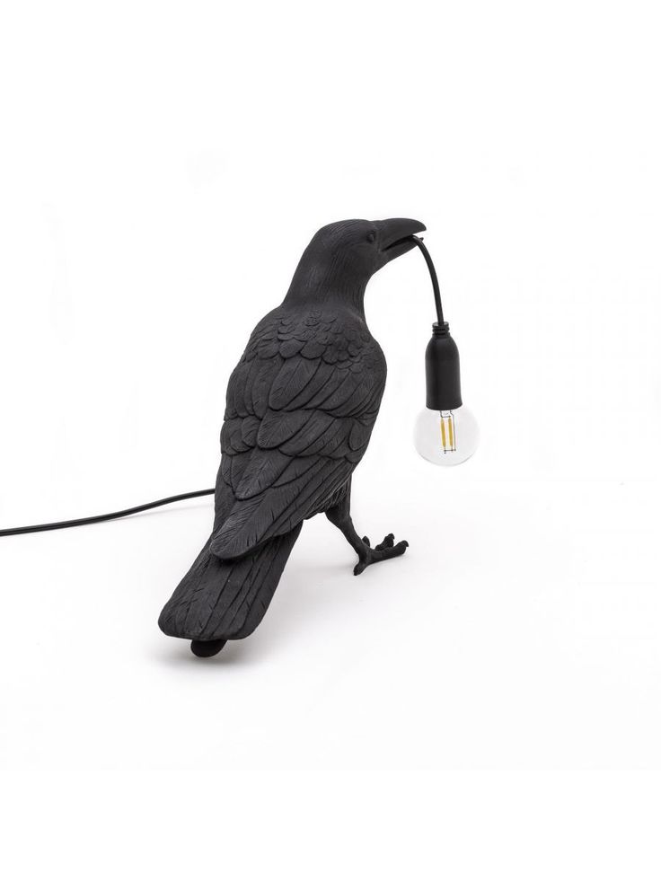 a black bird lamp sitting on top of a white table next to a light bulb