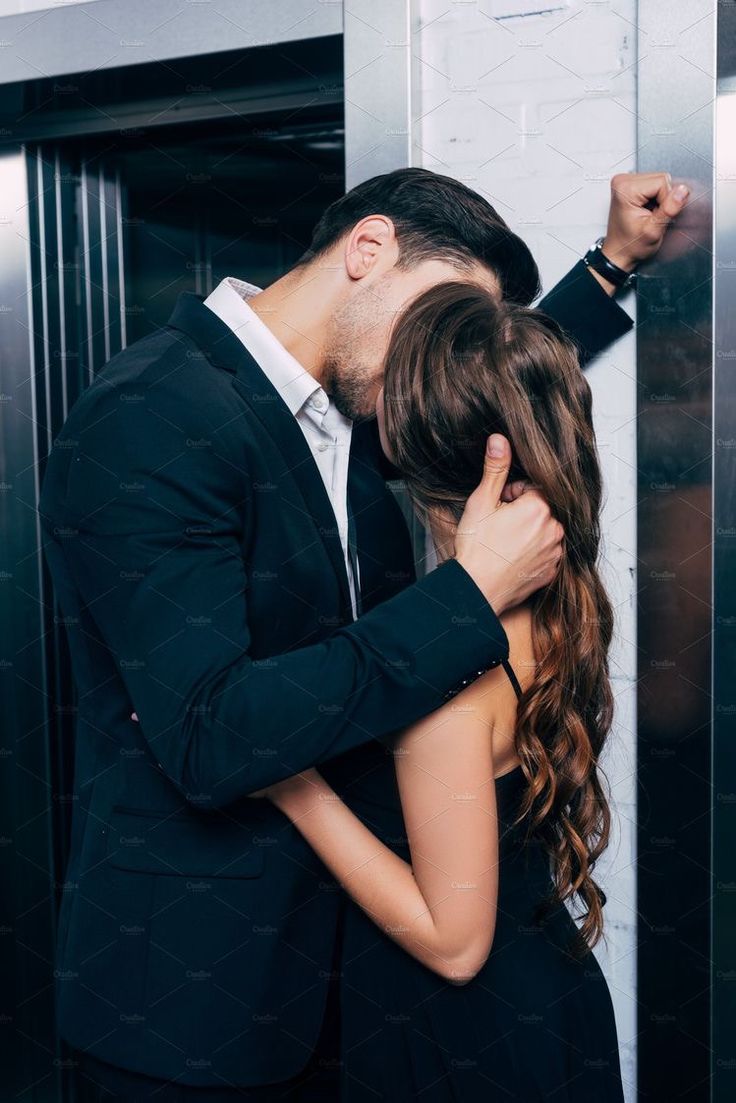 a man and woman kissing in front of an elevator door with their arms around each other