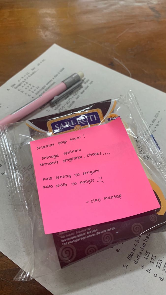 a pink sticky note sitting on top of a piece of paper next to a pen