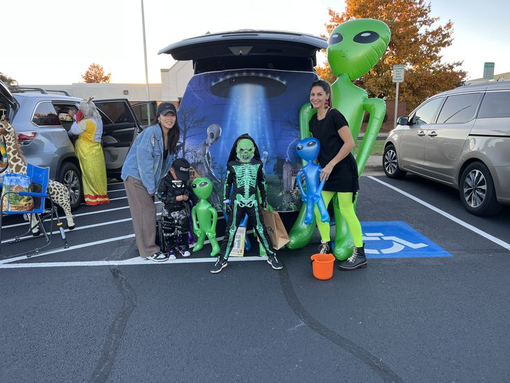 three people standing in front of a car with halloween decorations on the hood and back