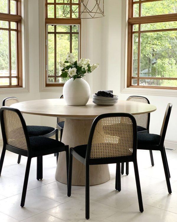 a dining room table with four chairs and a vase on the table in front of two windows