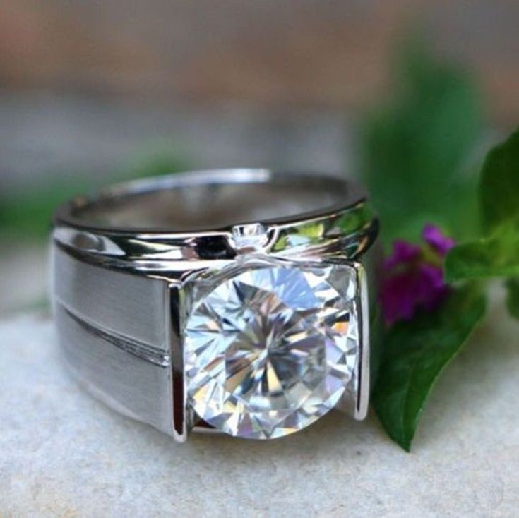 a diamond ring sitting on top of a white surface next to a purple flower and green leaves