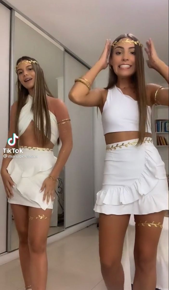 two women dressed in white and gold posing for the camera