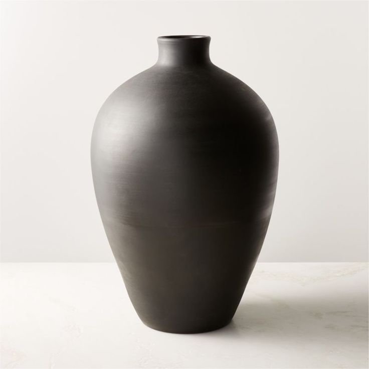 a black vase sitting on top of a table next to a white wall with a feather sticking out of it