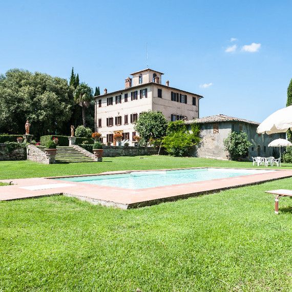 an outdoor swimming pool surrounded by lawn chairs and umbrellas in front of a large house