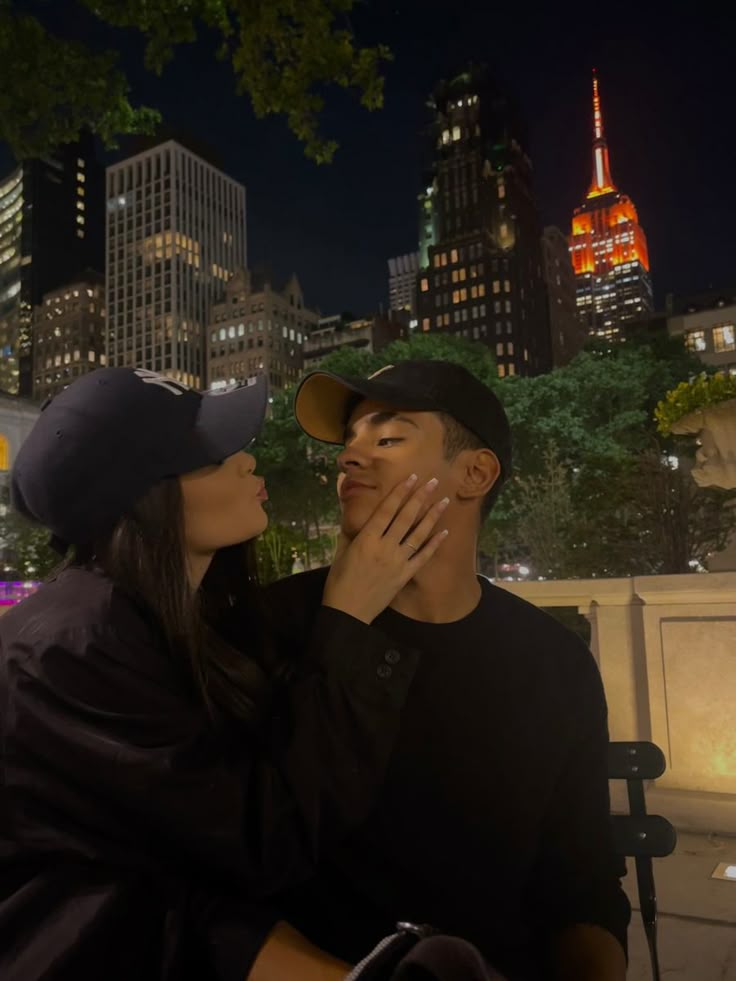 a man and woman sitting on a bench in front of a city skyline at night