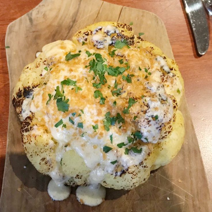 a wooden cutting board topped with an omelet covered in cheese and parsley