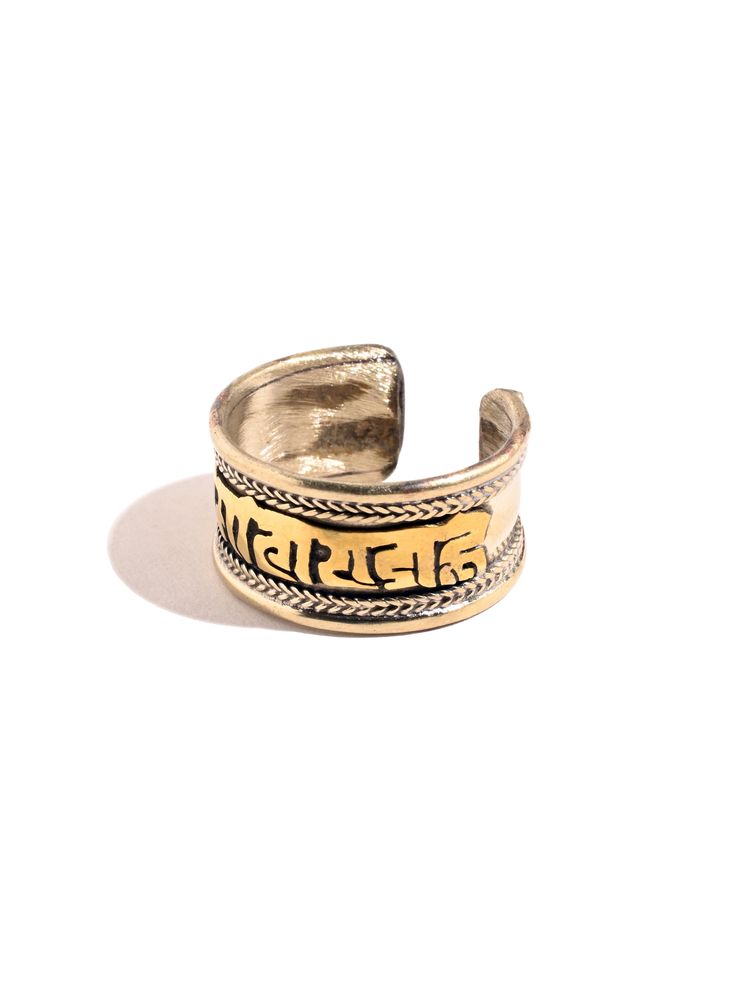 This adjustable ring is hand crafted by local artists of Nepal. It features the well known and oft chanted Tibetan holy mantra Om Mani Padme Hum artfully carved around the band, and a delicate rope like design decorating both sides. The brass ring can be gently pressed together to adjust to whichever finger on which you choose to wear it. Attractive and adjustable. Band measures almost 1/2 inch wide. Handcrafted in Nepal. Handmade Bohemian Open Engraved Ring, Handmade Bohemian Open Ring, Handmade Symbolic Toe Rings, Bohemian Adjustable Engraved Open Ring, Spiritual Style Adjustable Open Ring, Handmade Symbolic Engraved Ring For Promise, Symbolic Handmade Engraved Promise Ring, Symbolic Adjustable Brass Rings, Adjustable Gold Engraved Spiritual Ring