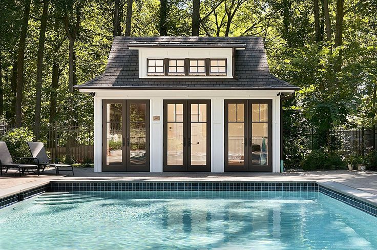 a small pool house with a swimming pool in the foreground and an outdoor lounge area on the far side