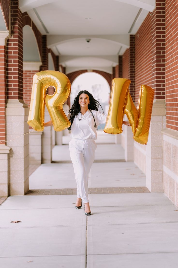 a woman in white holding up large gold balloons that spell out the word'm '