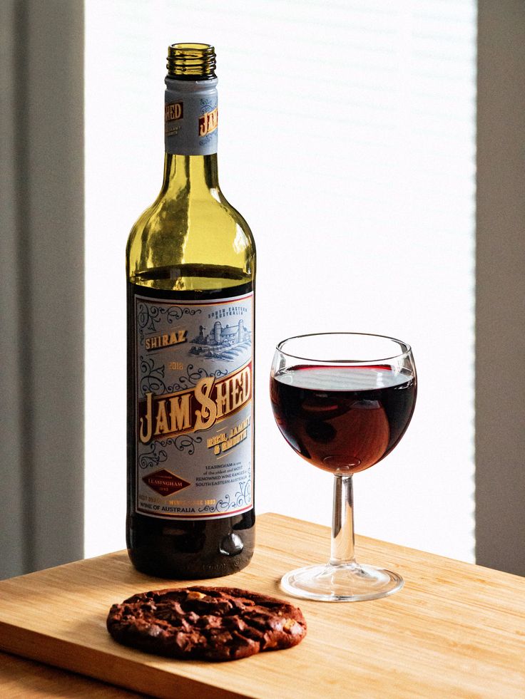 a bottle of wine sitting next to a glass on top of a wooden table with a cracker