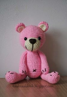 a pink crocheted teddy bear sitting on top of a wooden table next to a white wall