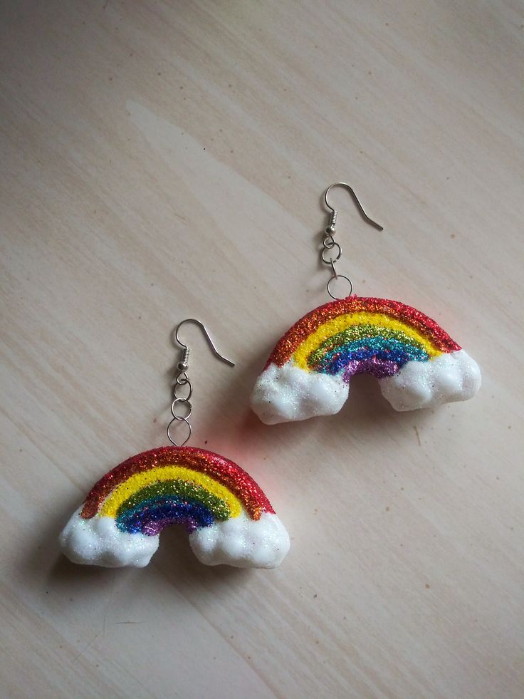 a pair of rainbow earrings on top of a wooden table with white clouds and red, yellow, green, blue, and purple colors