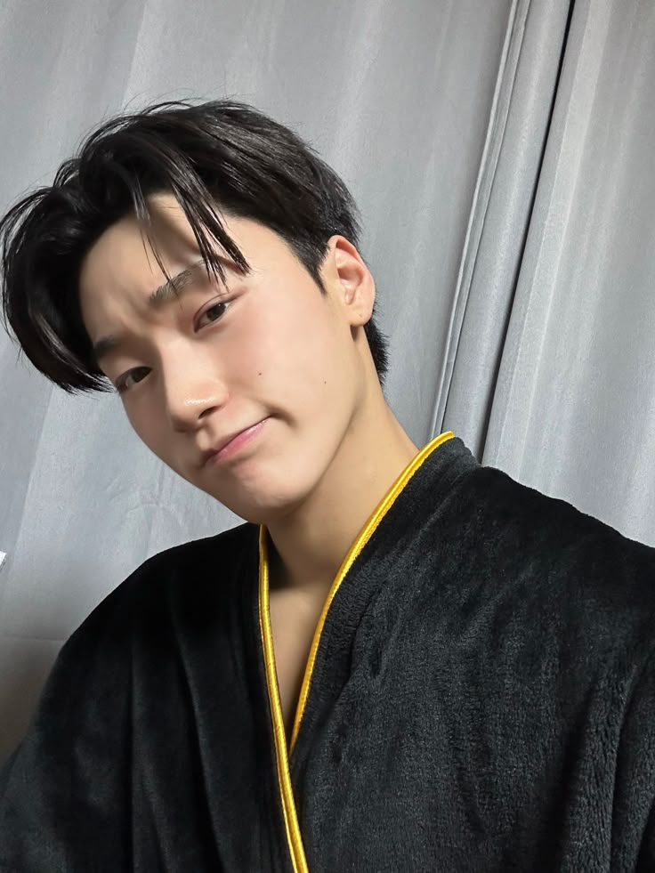 a young man with black hair wearing a robe and yellow necklace looking at the camera