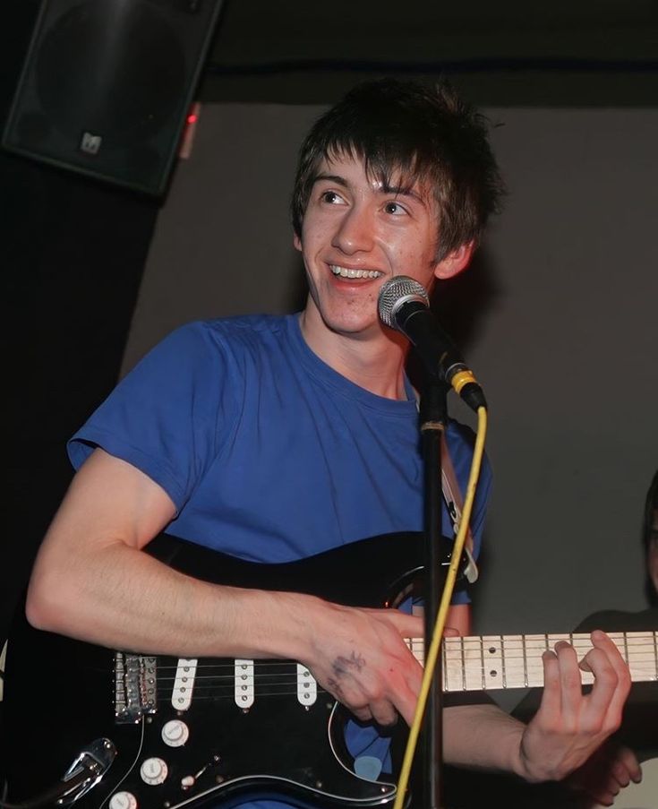 a young man holding a guitar and singing into a microphone