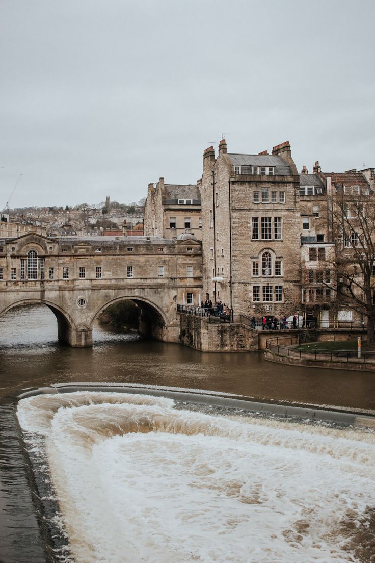 a boat traveling down a river next to a bridge with buildings in the back ground