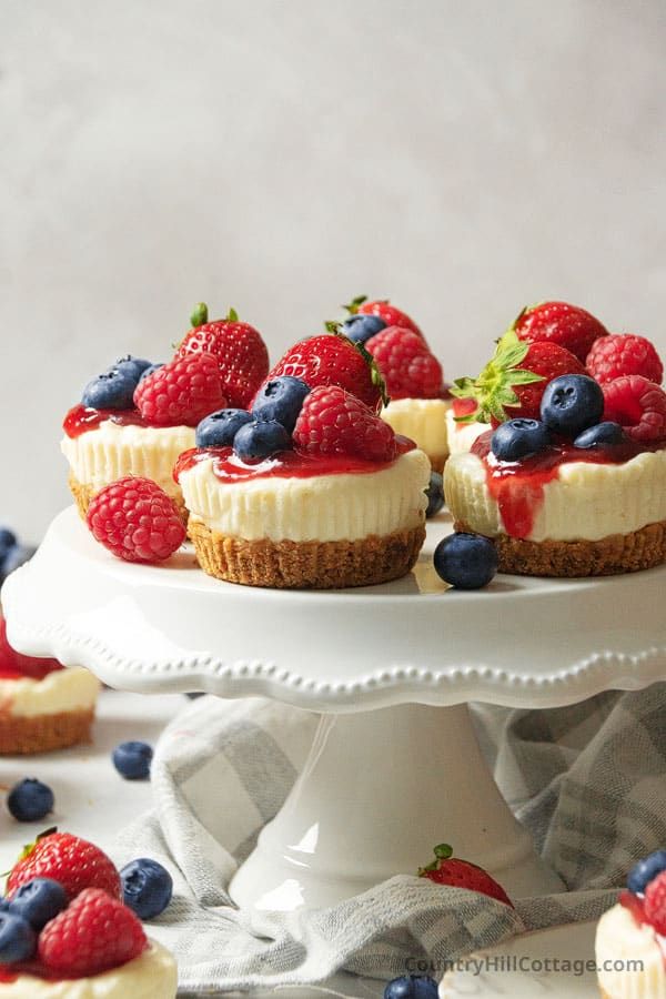 mini cheesecakes with berries and blueberries are on a cake plate surrounded by other small dessert items