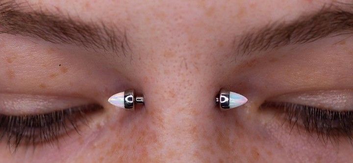 the eyes of a woman with two piercings on them