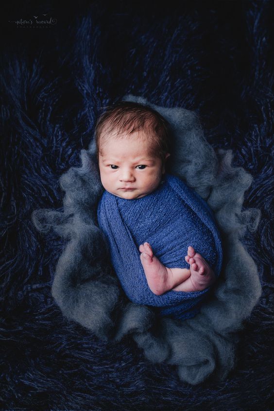 a baby wrapped in blue is laying on a fluffy blanket and smiling at the camera