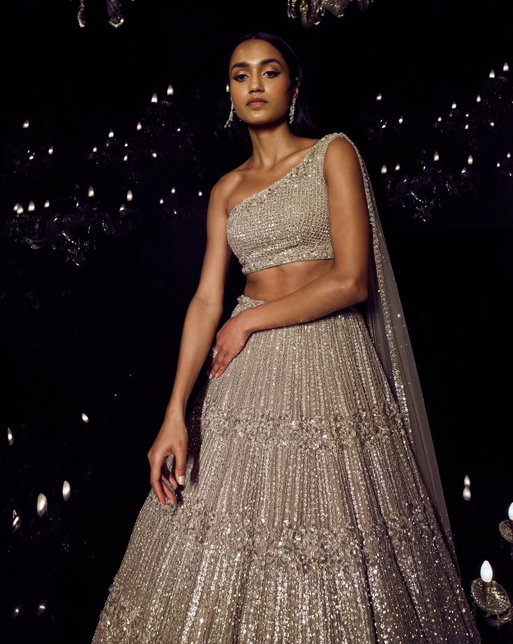 This champagne lehenga set features heavily embellished platinum cut sequin. The ensemble is paired with a one shoulder blouse with an attached net dupatta.From Seema Gujral's Tuscan Summer collection. DELIVERY TIMEPlease allow 4 months for your outfit to arrive. FABRIC DETAILSOrganza Professional cleaning only. One Shoulder Sequin Evening Sets, One Shoulder Sequin Set For Party, One-shoulder Sequin Set For Party, Bollywood One Shoulder Designer Wear Set, One-shoulder Lehenga For Festive Reception, Elegant One-shoulder Lehenga For Festive Occasions, One-shoulder Festive Lehenga For Reception, Festive One-shoulder Lehenga For Reception, Elegant One-shoulder Lehenga For Reception