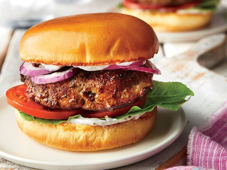 a hamburger with lettuce, tomato and onion on a white plate next to another burger