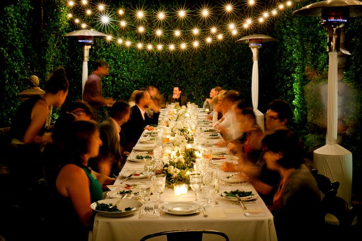 a group of people sitting around a long table with plates and wine glasses on it