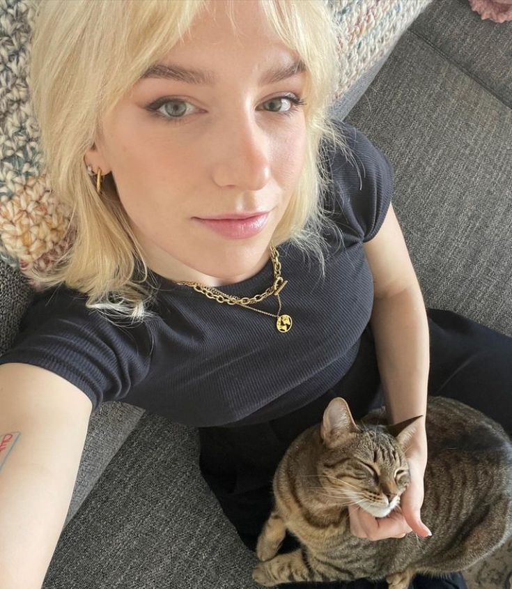 a woman sitting on a couch with a cat in her lap looking at the camera