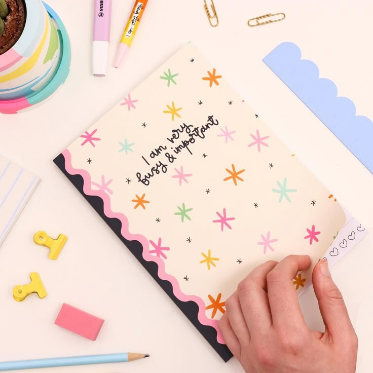 a hand holding a notepad on top of a desk next to some office supplies