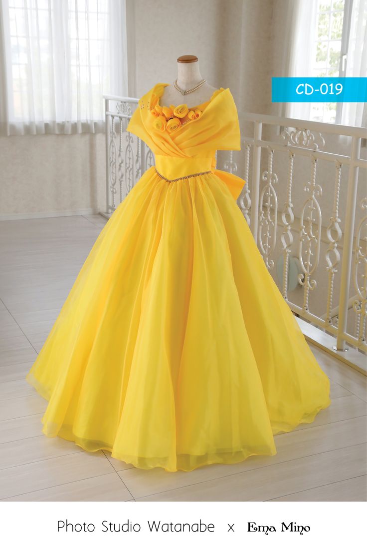 a yellow dress is on display in front of a white railing and windows with curtains