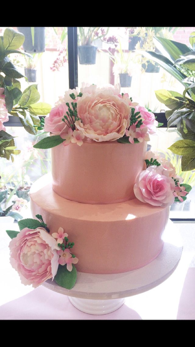 a three tiered cake with pink flowers on top and greenery in the background