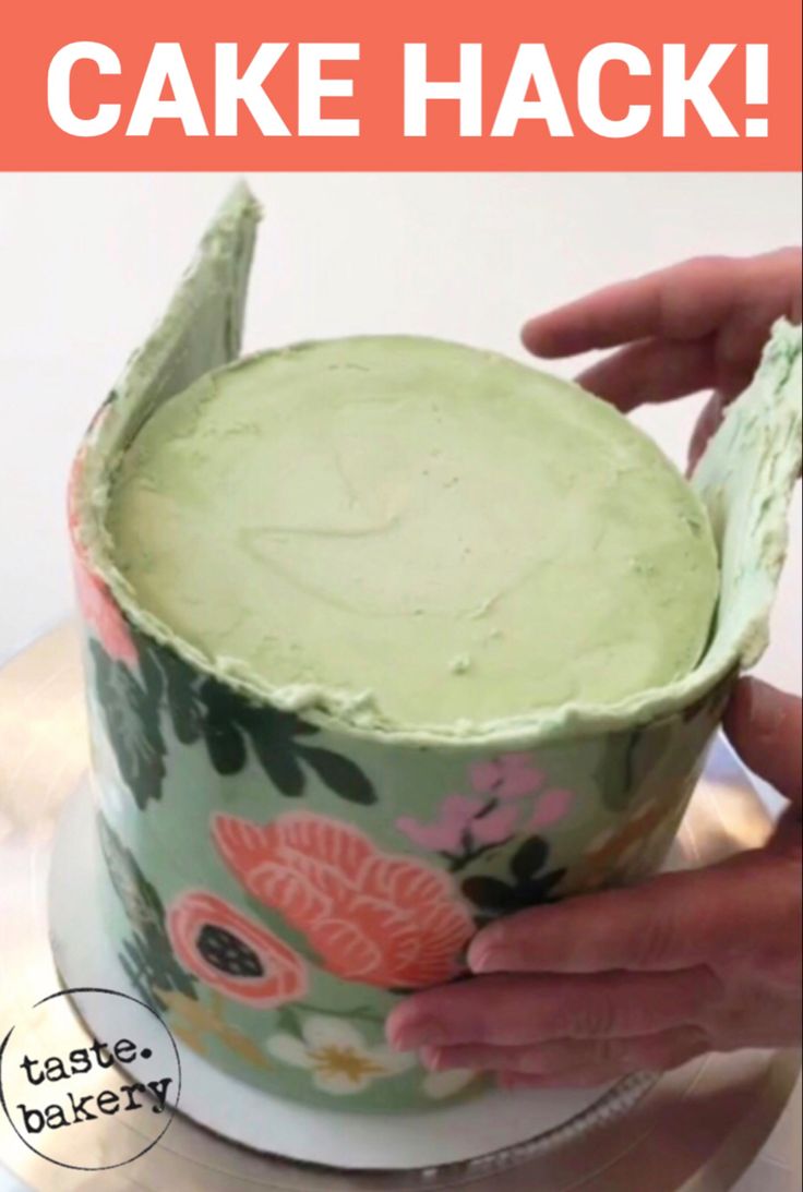 someone is decorating a cake with green icing and pink flowers on the top