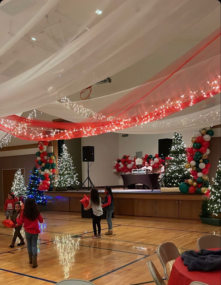 children are playing basketball in an indoor gym decorated with christmas trees and garlands on the ceiling