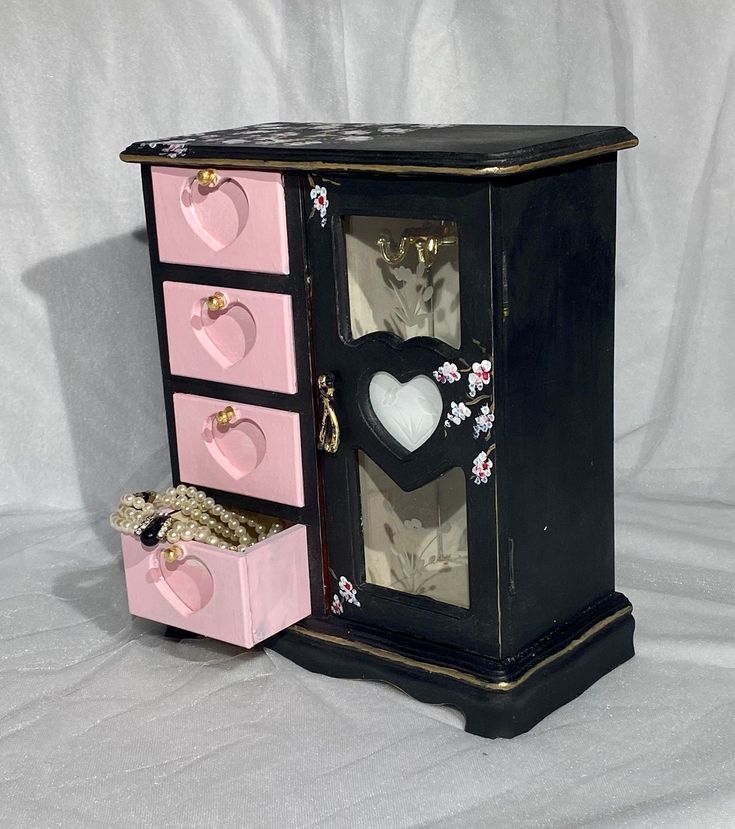 a small black and pink jewelry box with two hearts on it's sides, sitting next to a white background