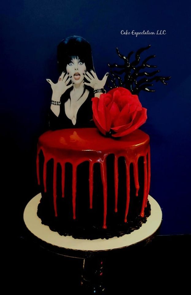 a red and black cake with dripping icing on the top, featuring a woman holding her hands up to her face