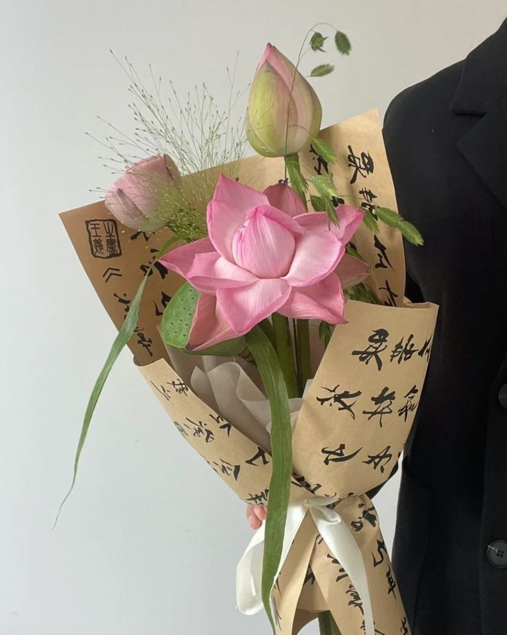 a bouquet of pink flowers wrapped in brown paper with writing on it and tied to a mannequin's torso