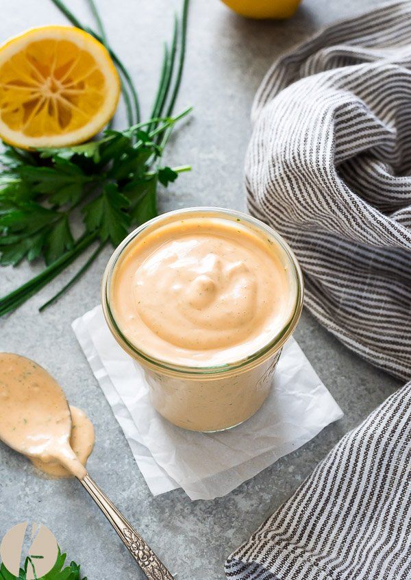 a glass jar filled with peanut butter and topped with fresh herbs next to a spoon