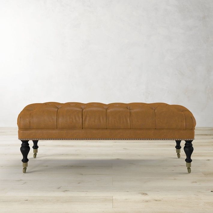 an upholstered leather bench with wooden legs and nail polishing on the legs