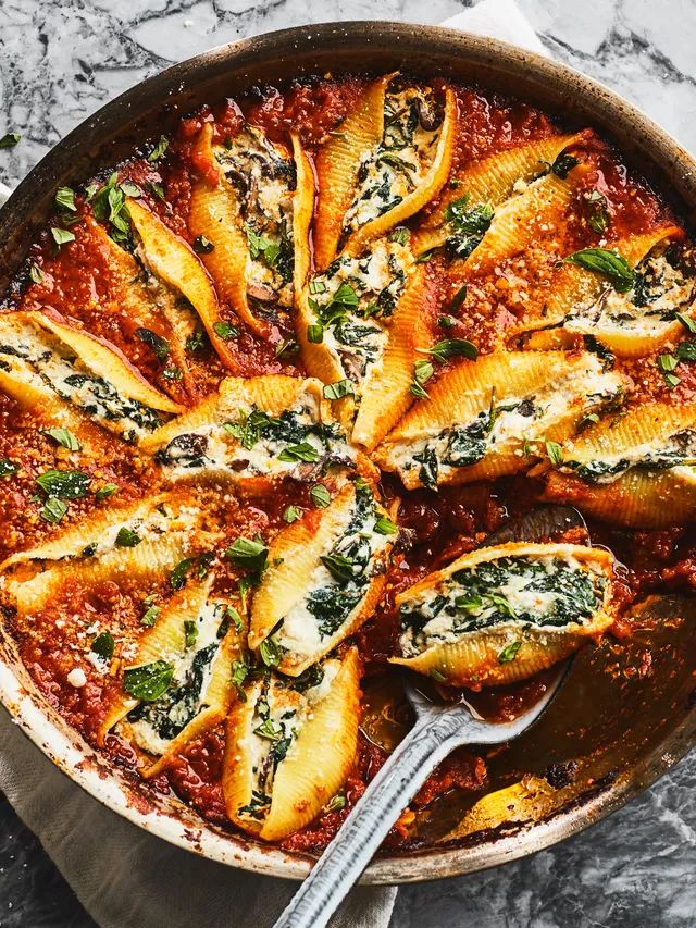 a skillet filled with ravioli and spinach covered in sauce on top of a marble counter