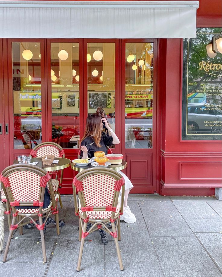 two people sitting at an outdoor cafe table outside the storefront with food on it