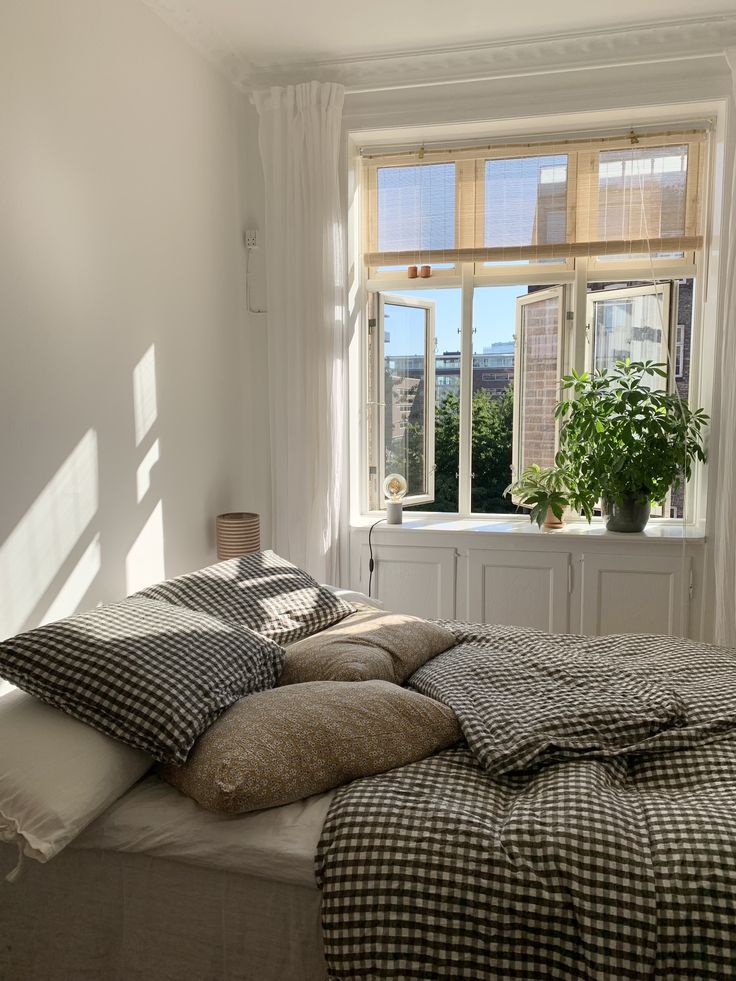 a bed sitting in front of a window with pillows and blankets on top of it