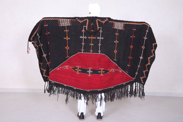 "A rare and authentic Berber shepherd's hooded cape or shawl (salham) that ranks among the most magnificent weavings in Morocco. Made by the Ait Ouaouzguite tribe, the akhnif has two major design sections: the first is the black plainwoven field decorated with Berber talismanic tattoos and symbols. The second is the red 'half moon' or eye as protection against the evil eye. The motif in the centre is that of a lizard, which with its sharp tongue pierces evil. Handwoven on an upright loom from go Traditional Black Cape For Festival, Traditional Black Festival Cape, Traditional Alpaca Winter Cape, Bohemian Brown Cape Shawl, Bohemian Red Shawl Cape, Handwoven Winter Shawl Cape, Bohemian Handwoven One-size Cape, Sharp Tongue, Tongue Piercing