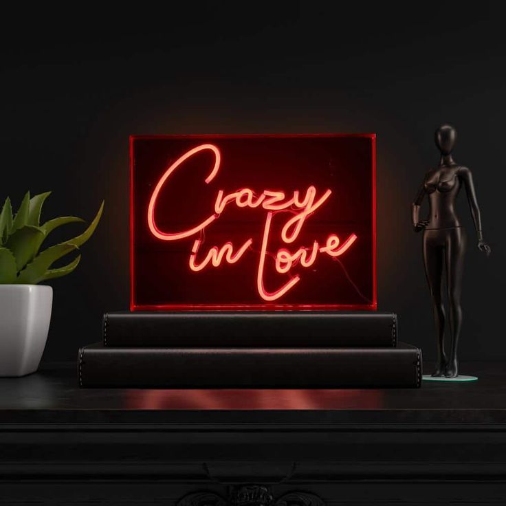 a neon sign that says crazy on love next to a mannequin and potted plant