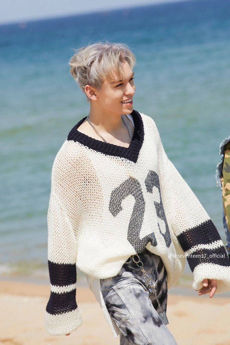 a woman walking on the beach wearing a white sweater with black and grey numbers printed on it