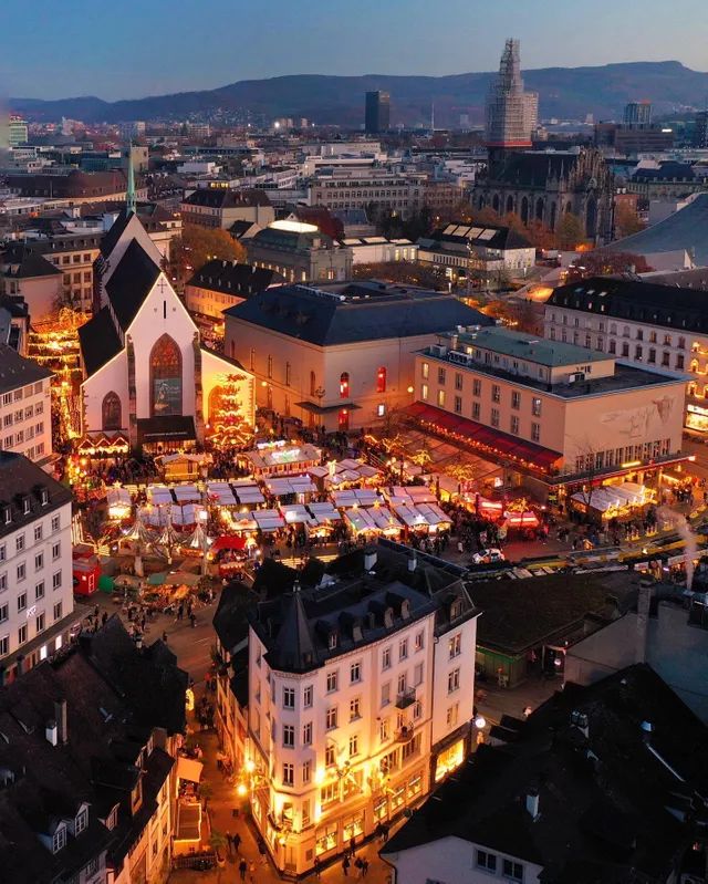 an aerial view of a city at night with buildings lit up and people walking around