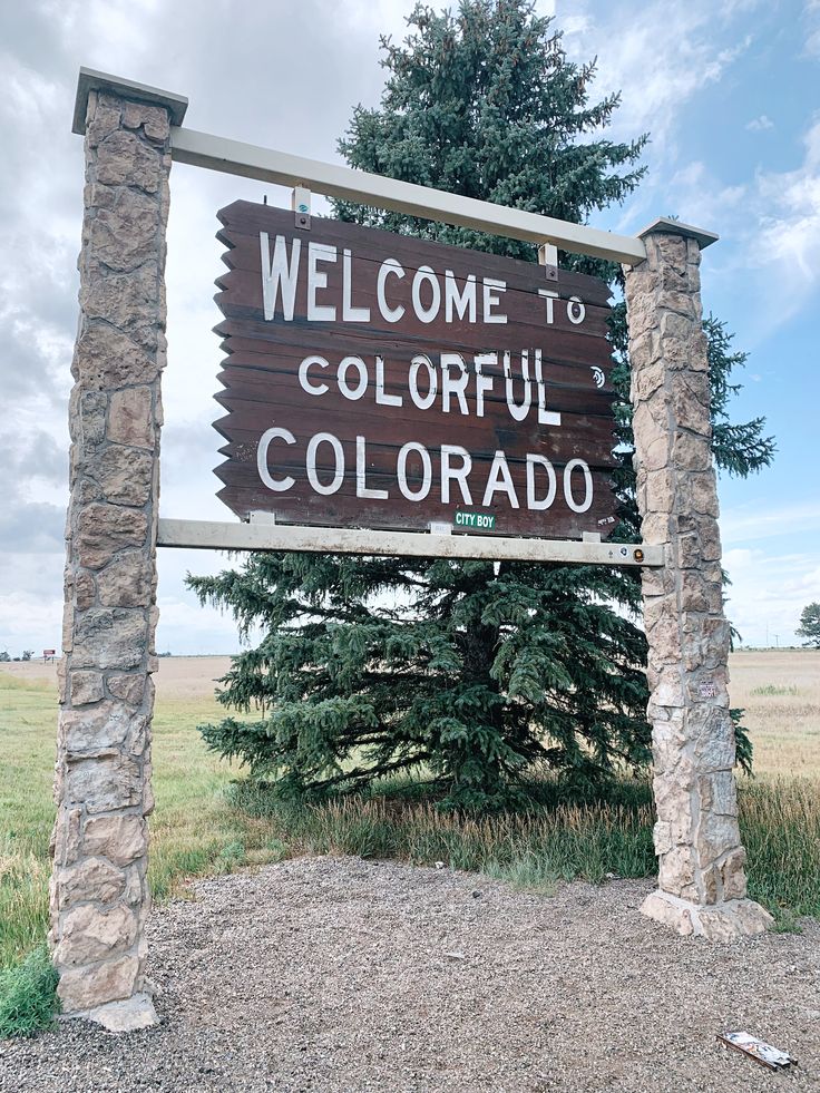 a welcome sign to the state of colorado in front of a field with trees and grass