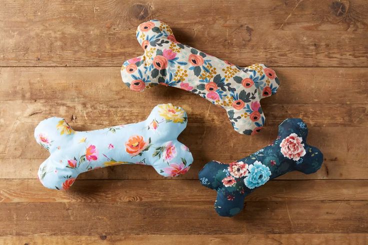 three dog bone ornaments on a wooden floor with floral fabric and wood planks in the background