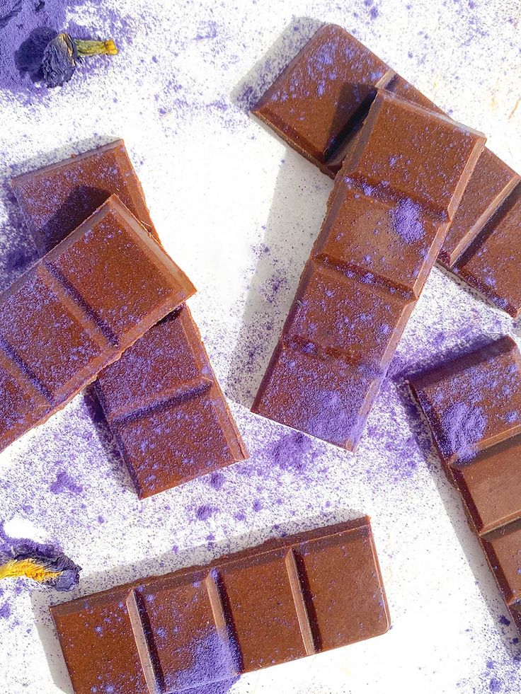 several pieces of chocolate sitting on top of a table covered in purple powder and sprinkles