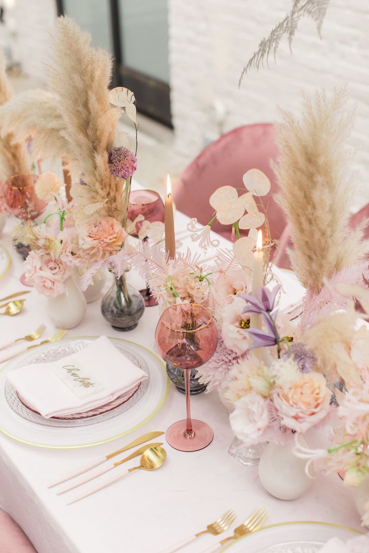 the table is set with pink flowers and gold place settings for an elegant dinner party