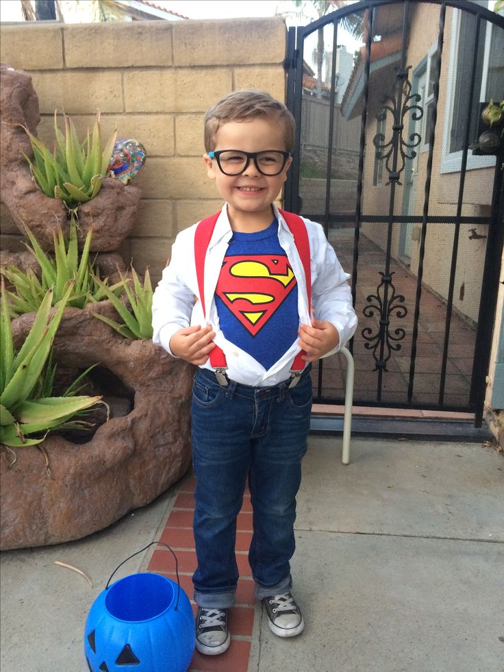 a young boy wearing a superman t - shirt standing in front of a gate with a blue bucket