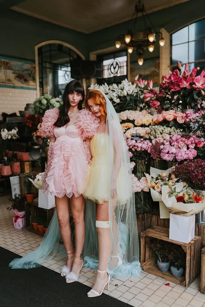 two women standing next to each other in front of flower shop with pink and yellow flowers